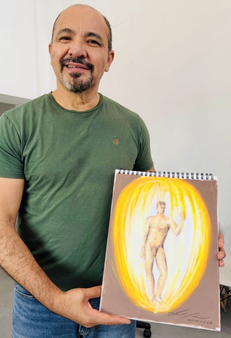 Víctor Ayala sostiene una obra pictórica de figura humana rodeada por luz amarilla